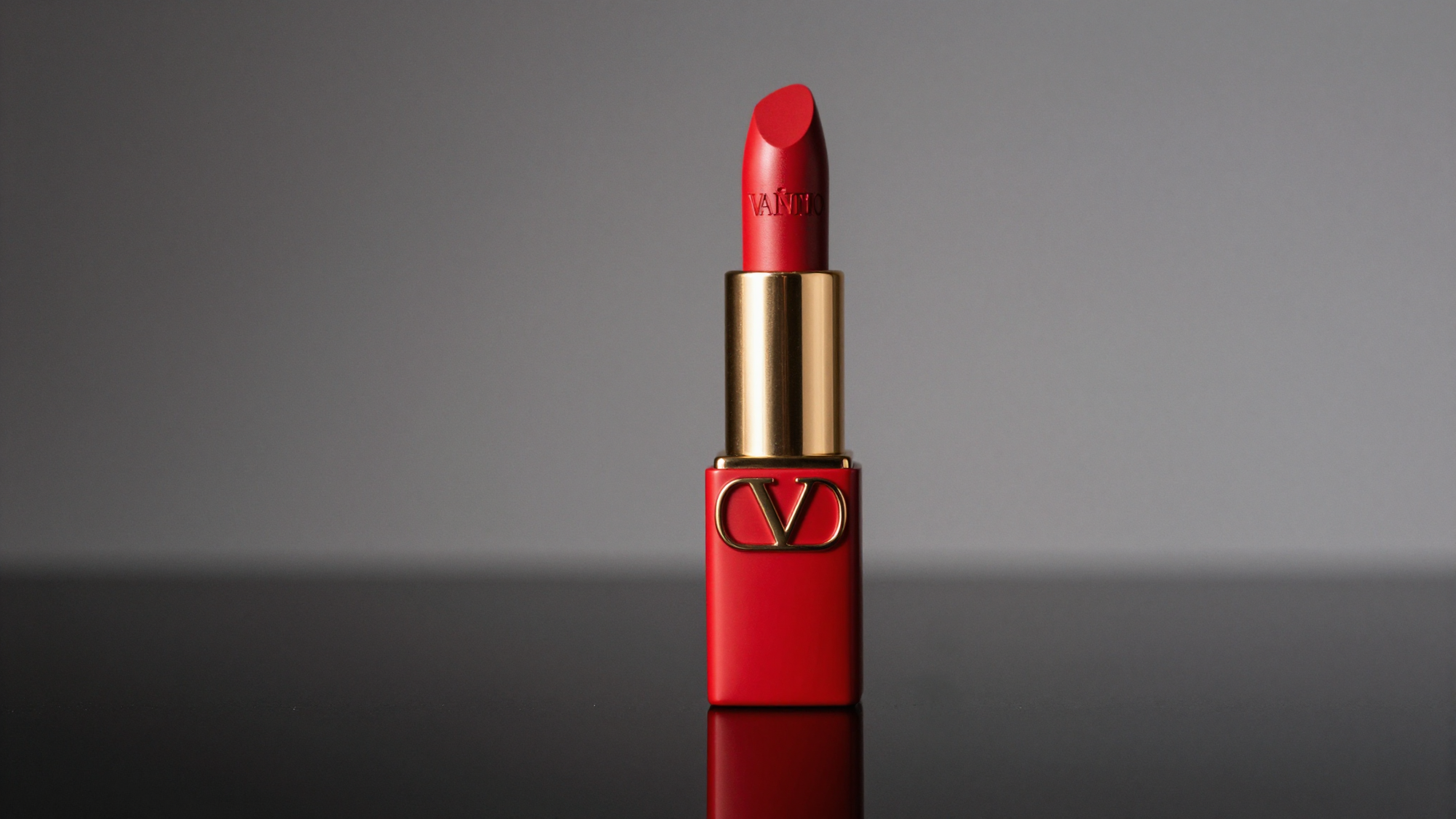 Close-up of a Valentino lipstick in a red and gold case on a reflective surface.