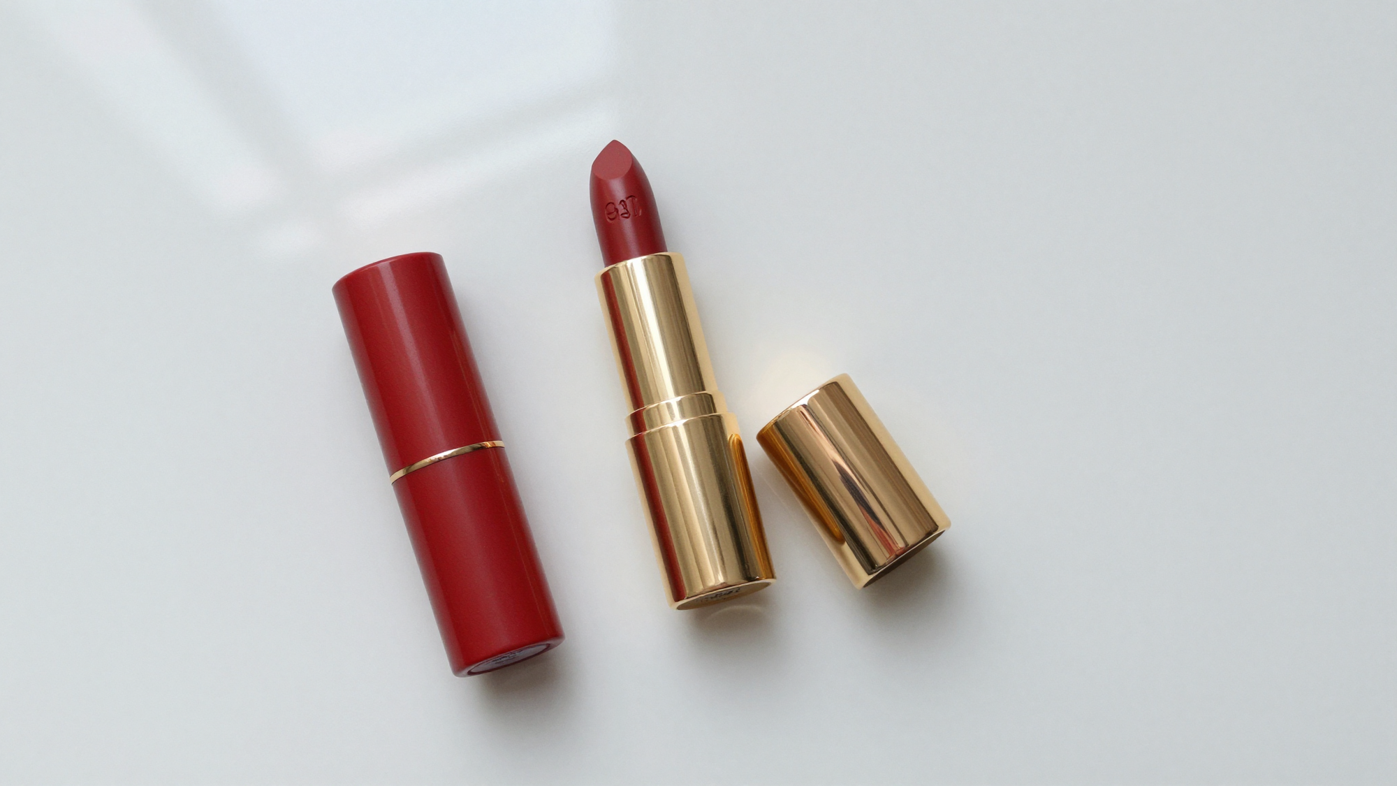 Flat lay of a red lipstick case with gold accents on a glossy white surface