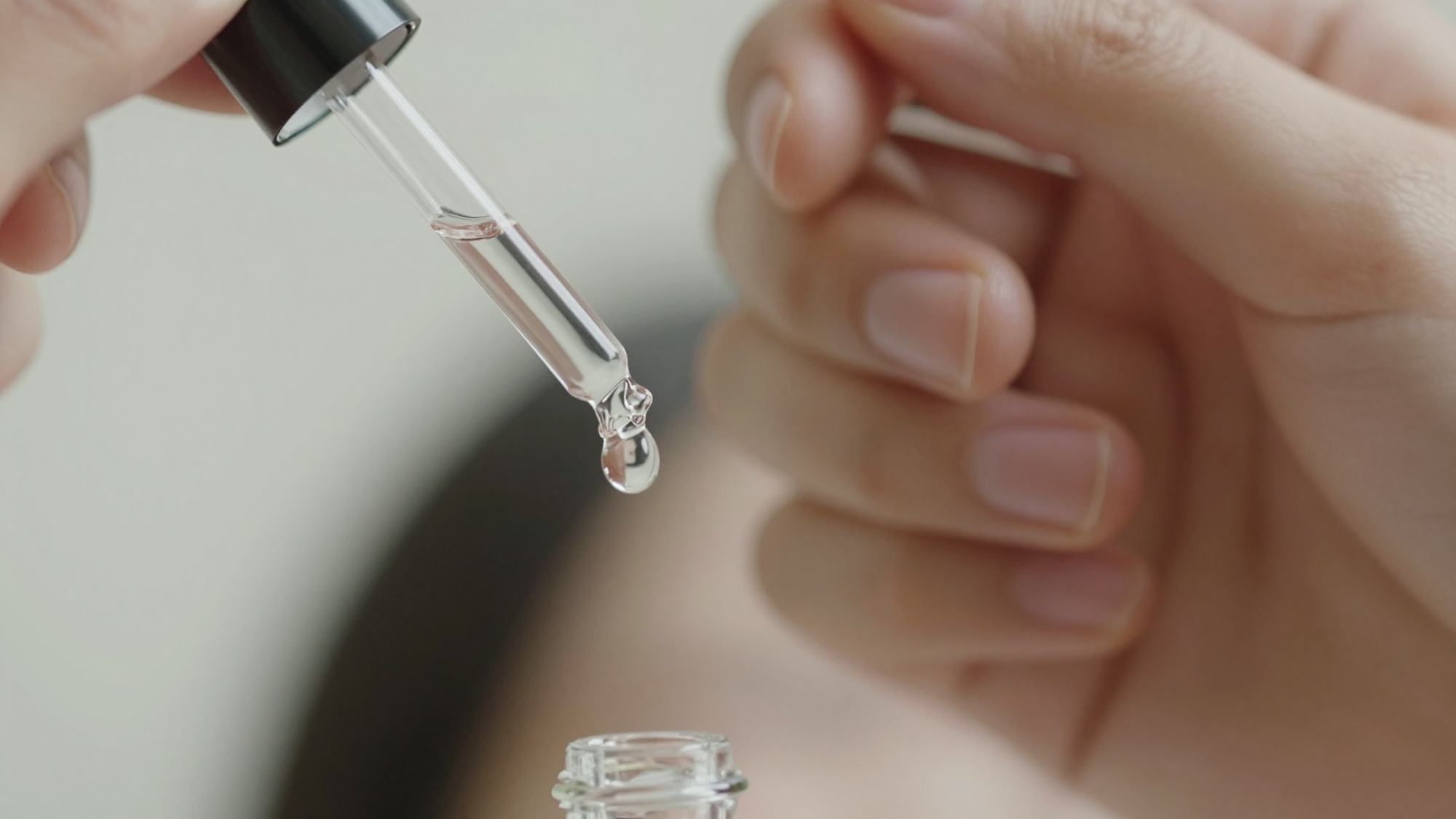 Close-up of a hand holding a dropper, a drop of serum suspended at the tip
