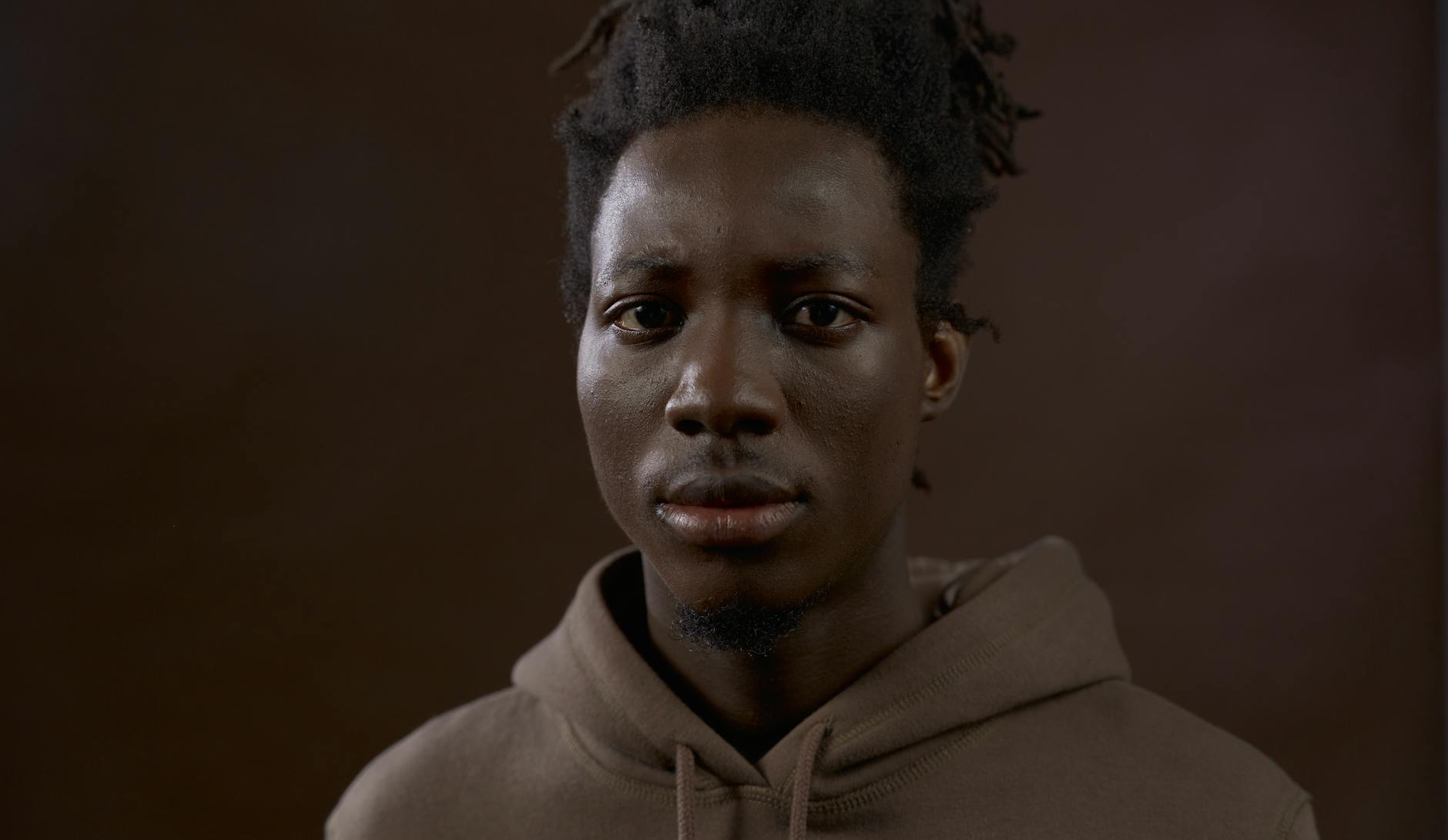 Studio portrait of a young man with a brown background, expressing serious emotion.