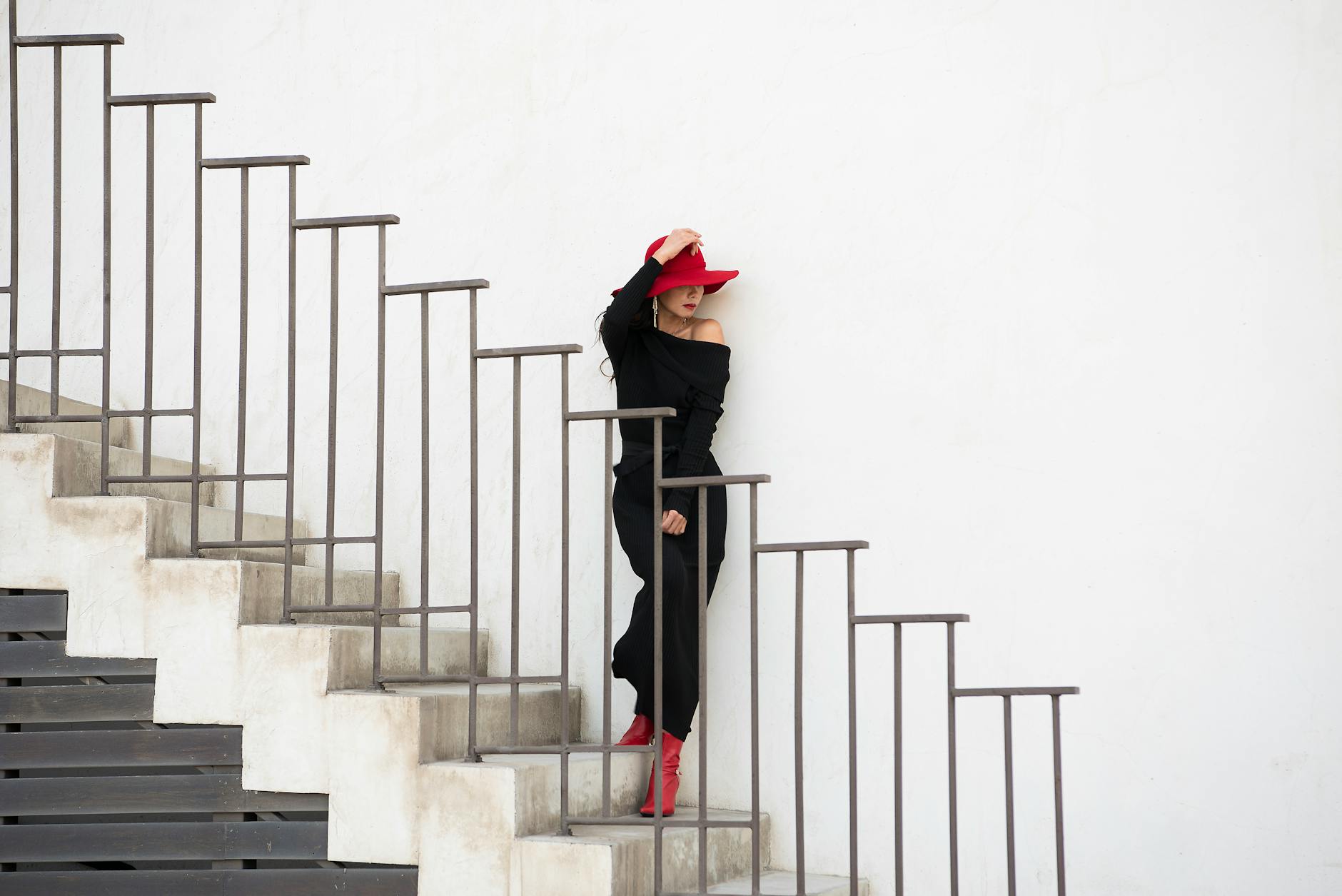 Elegant woman in black with a red hat poses stylishly on a modern staircase