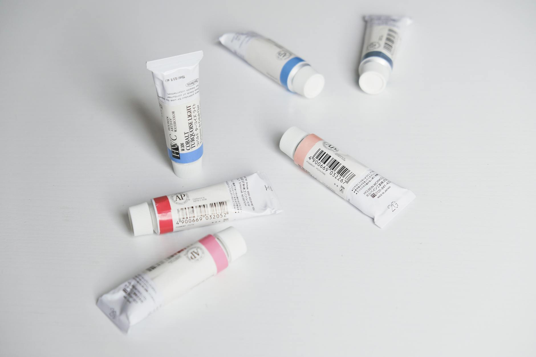 Close-up of colorful paint tubes arranged on a white surface in a flat lay style.