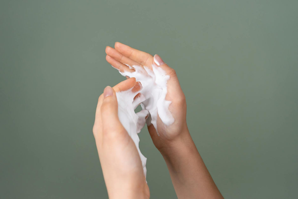 Close-up of hands applying rich moisturizing cream on a green background.
