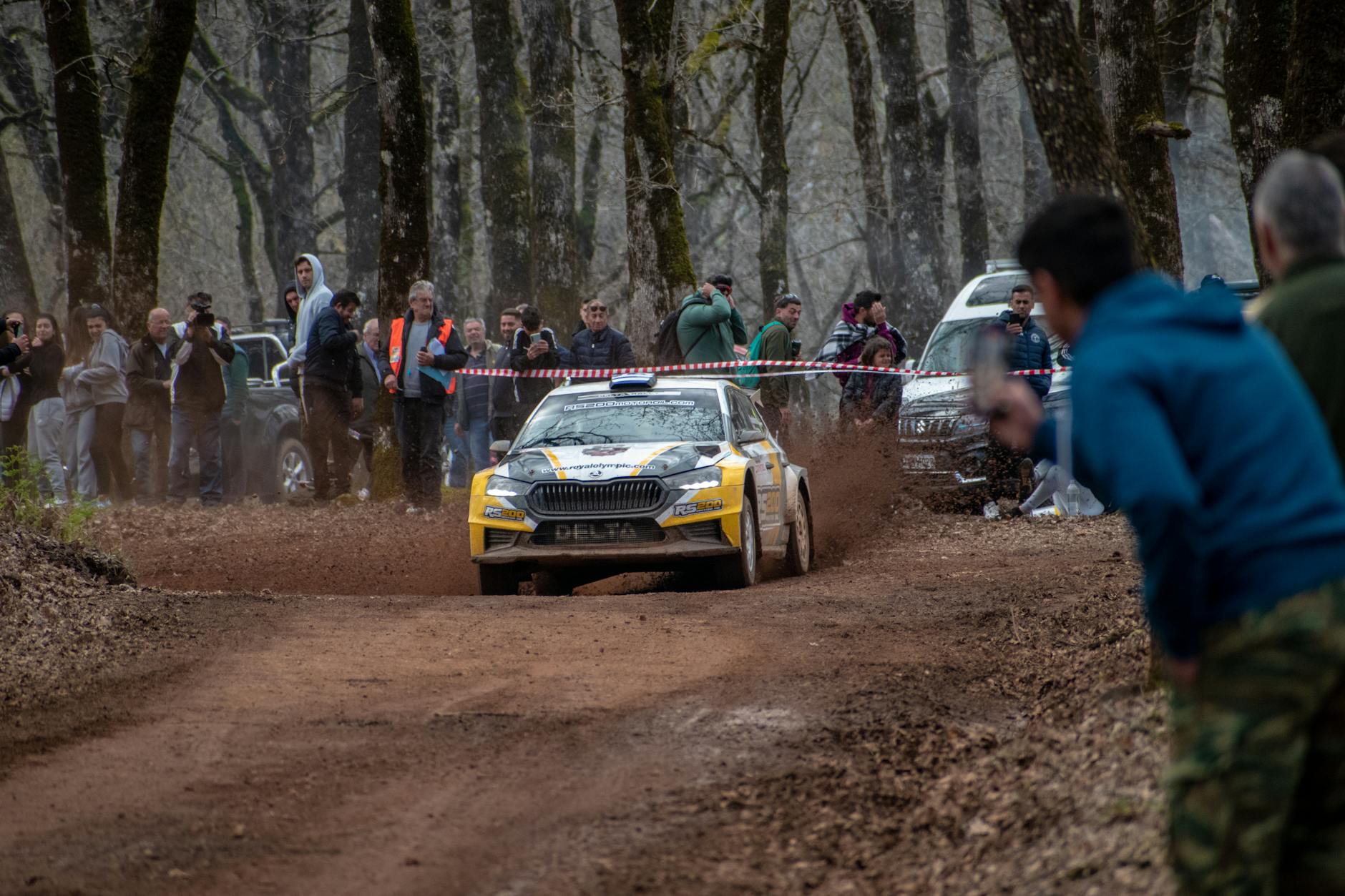 Exciting rally car event with spectators on a dirt track in Ilia, Greece, showcasing motorsport action.