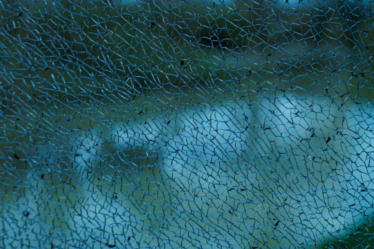 Detailed close-up image of shattered glass with intricate blue pattern against blurry background.