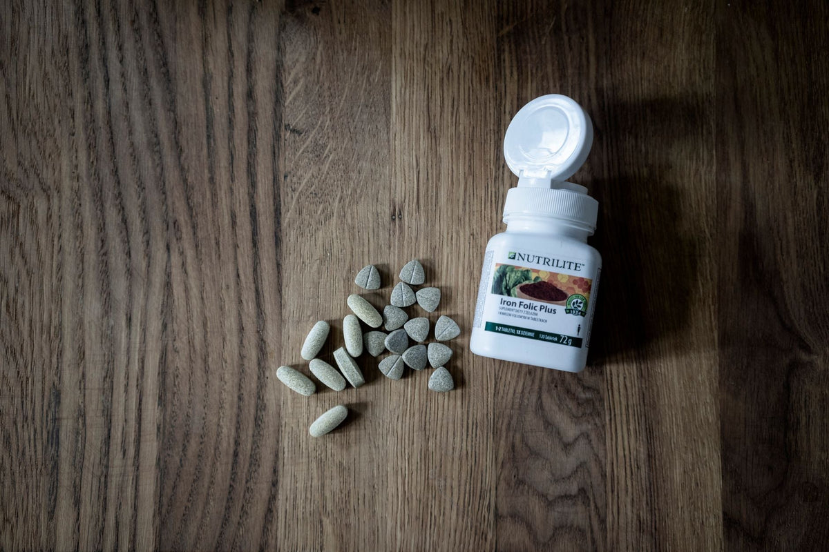 Top view of set of various medical pills near plastic container placed on wooden table