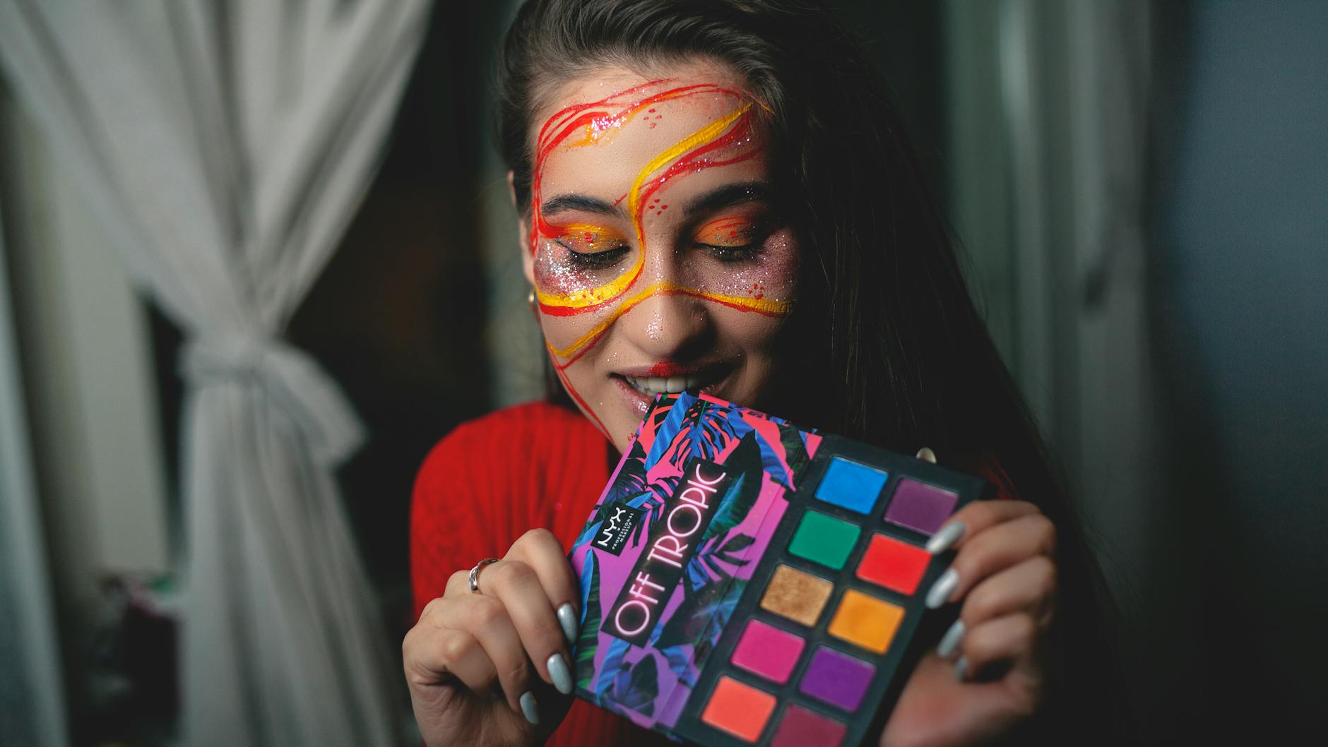 A woman showcasing artistic face makeup with a colorful palette indoors.