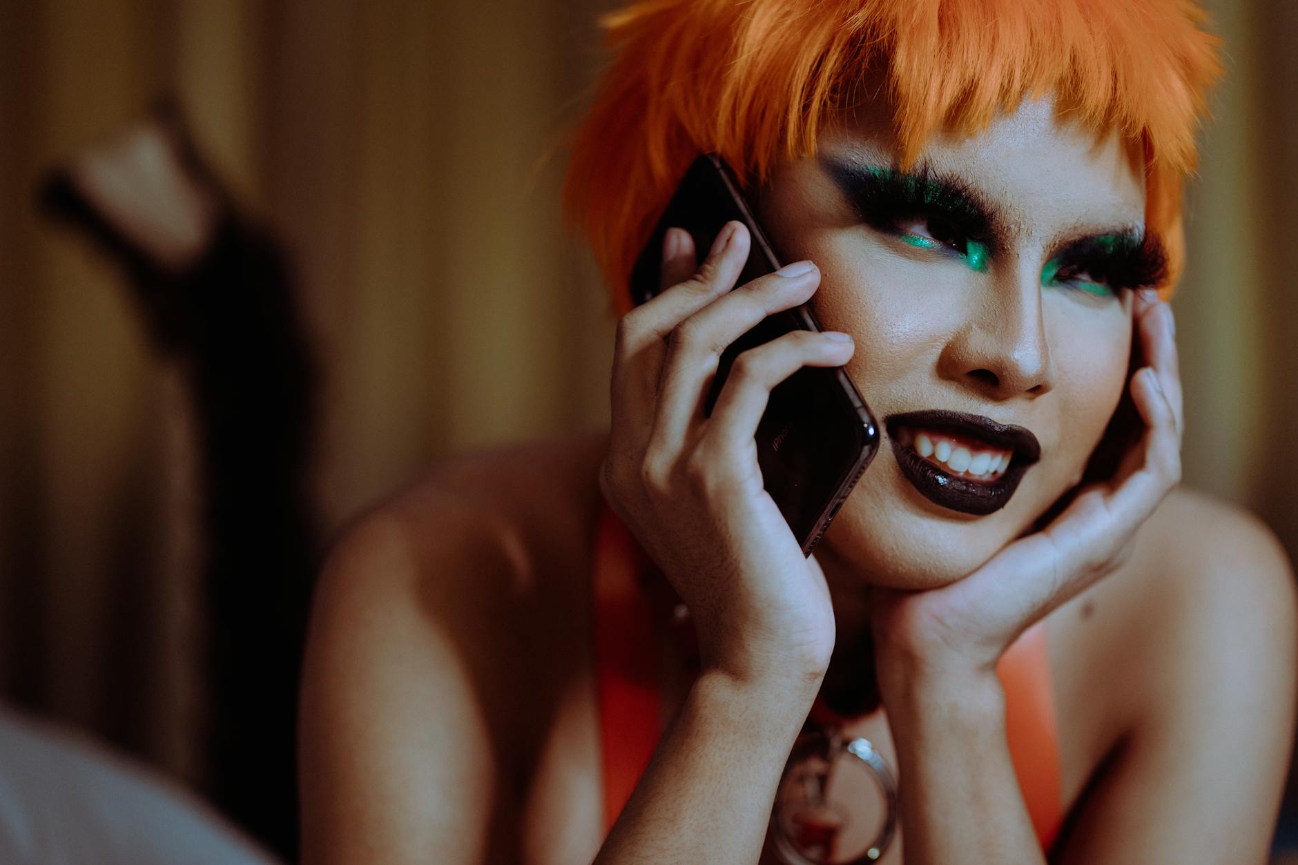 A vibrant drag performer chatting on a phone with striking makeup and funky style.