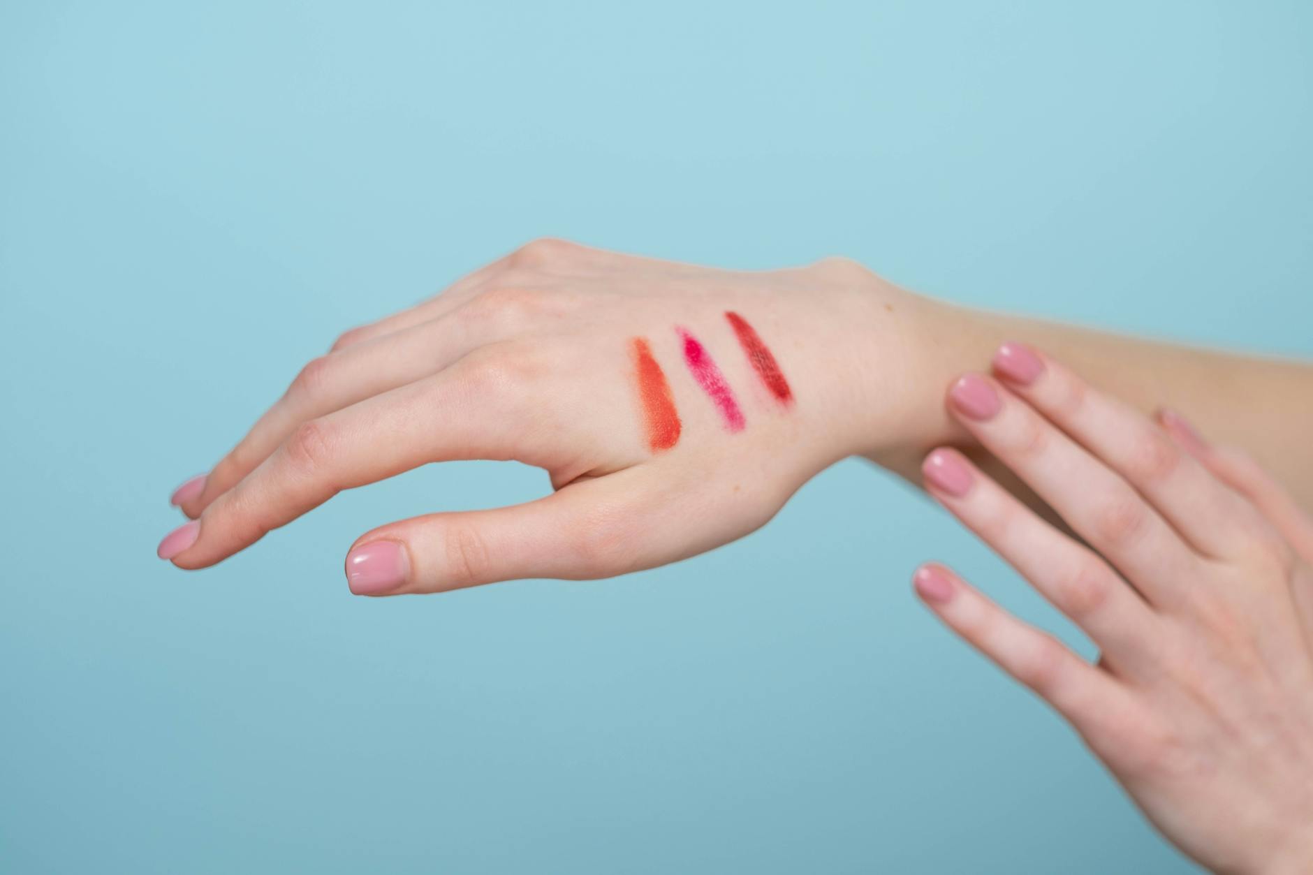 Close-up of lipstick swatches on a woman's hand against a blue background.